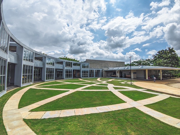 Curved glass-fronted building around a lawn cut through with pale stone paths