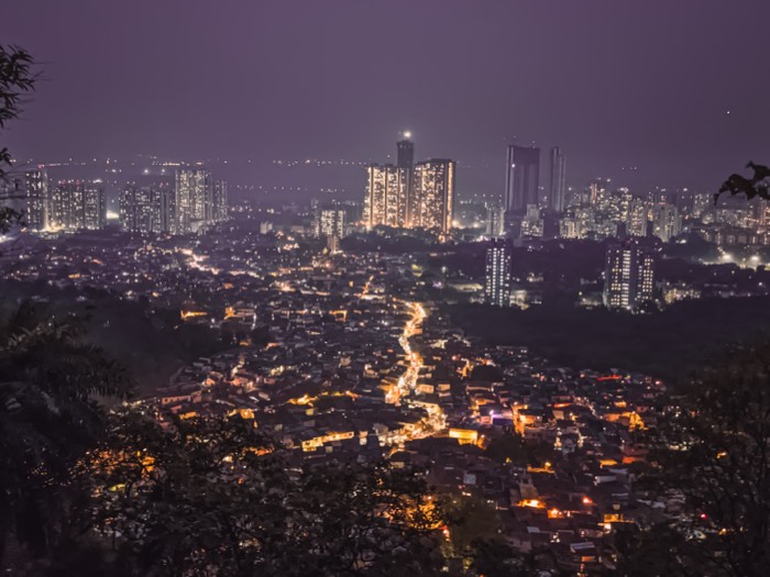 Mumbai at night seen from a hillside, lit towers rising above dense low rooftops