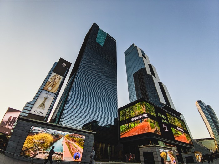 Glass skyscrapers seen from below, with large advertising screens at street level