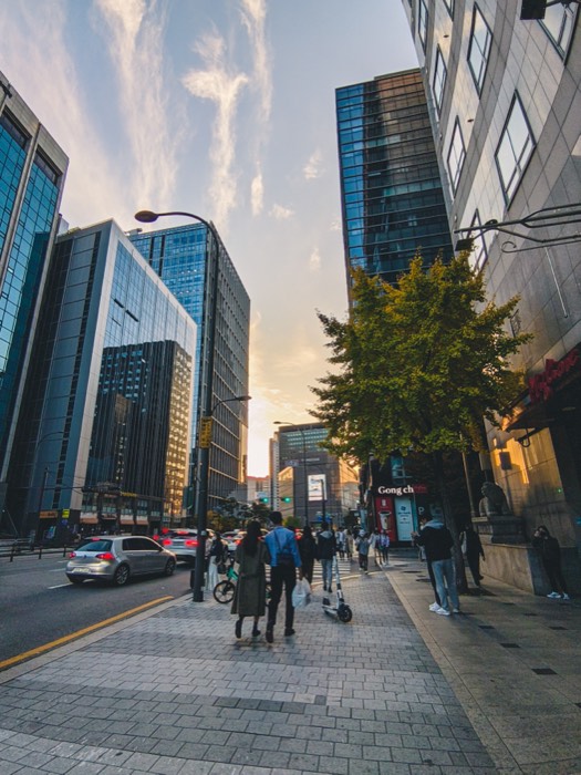 Seoul street in late afternoon light, pedestrians crossing between office towers