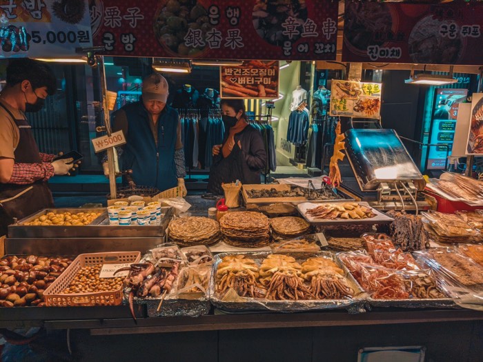 Market stall spread with roasted chestnuts, dried squid and pancakes under Korean signage
