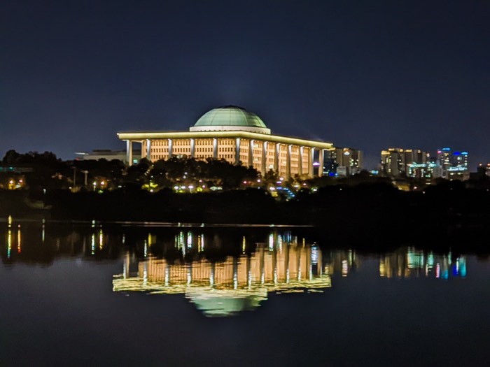 The domed National Assembly building lit up at night, reflected in the river