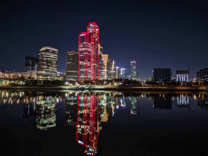 City skyline at night, a red-lit tower mirrored in dark water