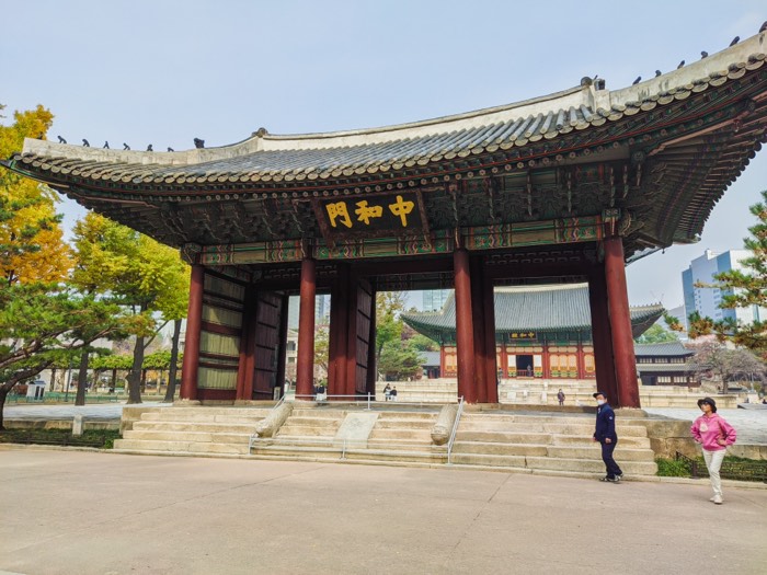 Junghwamun, the ornate wooden gate of Deoksugung Palace, with birds lined along its tiled roof