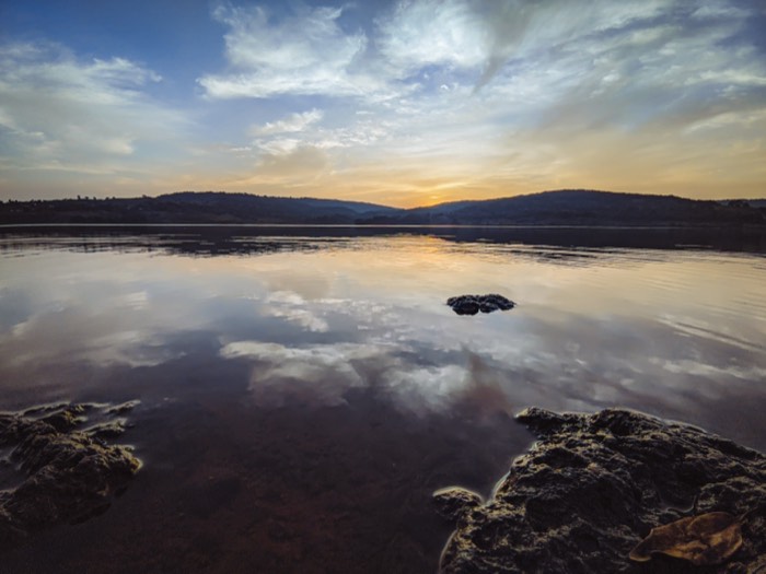 Clouds mirrored in the glassy surface of a lake at sunset, hills on the far shore